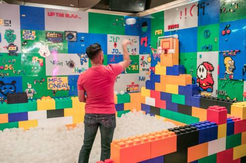 A person throws a ball towards a basketball hoop in a colorful room decorated with LEGO bricks and pixel art.