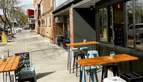 Outdoor seating area with wooden tables and metal chairs beside a building, featuring a sign for wine slushies.