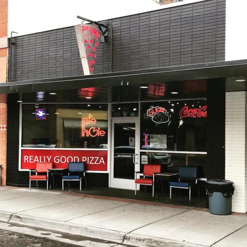 Exterior of a pizza restaurant with neon signs, featuring a red banner that says "REALLY GOOD PIZZA."