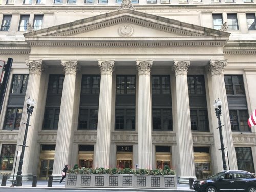 A grand building with tall columns and large windows, featuring a decorative facade and planters in front.