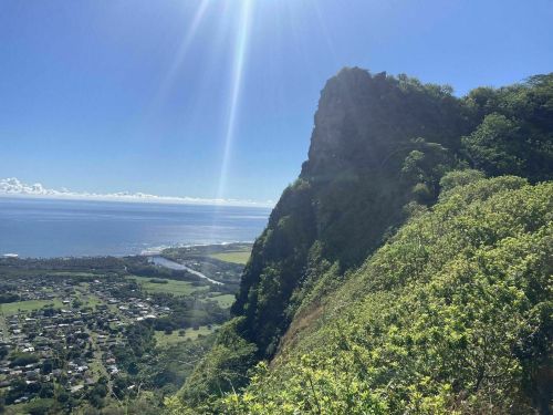 A scenic view of a rocky cliff overlooking a coastal landscape and ocean under a bright blue sky.