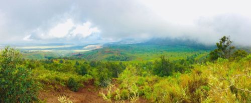 A panoramic view of lush green hills under a cloudy sky, with distant mountains and valleys visible in the background.
