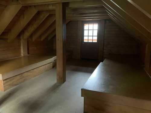 A dimly lit attic with wooden beams, two built-in benches, and a door leading outside.