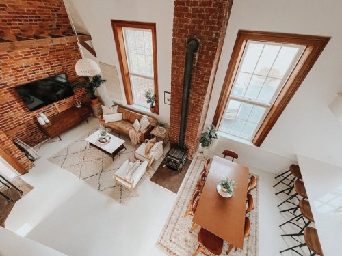 A cozy, modern living space with exposed brick walls, a dining area, and large windows, featuring stylish furniture.