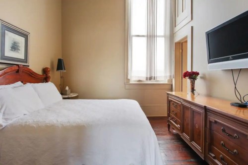 Cozy bedroom with a wooden bed, dresser, TV, and large window letting in natural light.