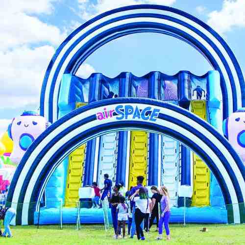 A colorful inflatable slide with children playing around it on a sunny day.