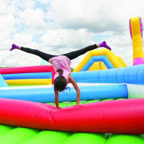 A girl performs a handstand on a colorful inflatable bounce house under a cloudy sky.