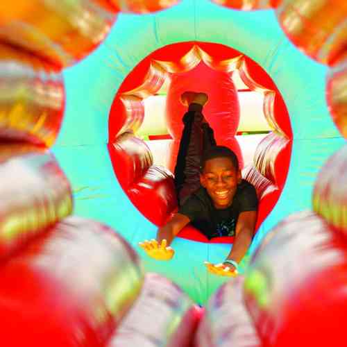 A joyful child slides through a colorful inflatable tunnel, smiling with arms outstretched.