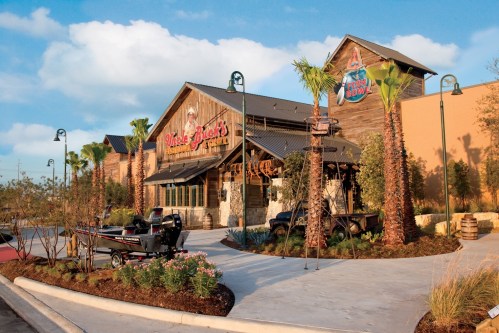 Exterior of a rustic restaurant with palm trees, a boat, and a welcoming entrance under a blue sky.