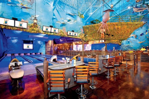 A vibrant bowling alley with an underwater theme, featuring colorful murals, seating, and screens.