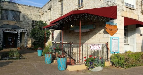 A stone building with a red awning, potted plants, and an "OPEN" sign at the entrance.