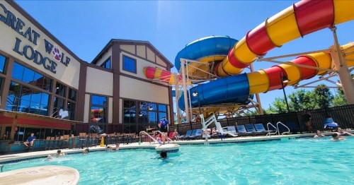 A vibrant water park scene at Great Wolf Lodge, featuring a large water slide and guests enjoying the pool.