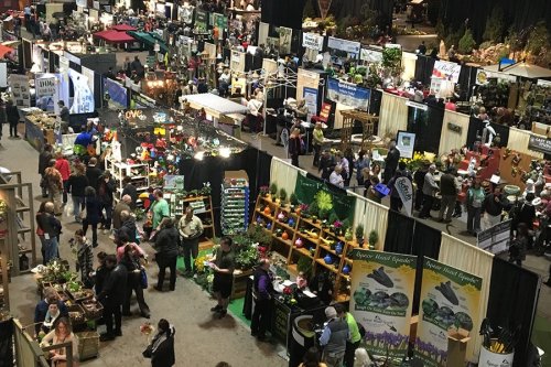A bustling indoor event with numerous booths, vendors, and visitors exploring various displays and products.