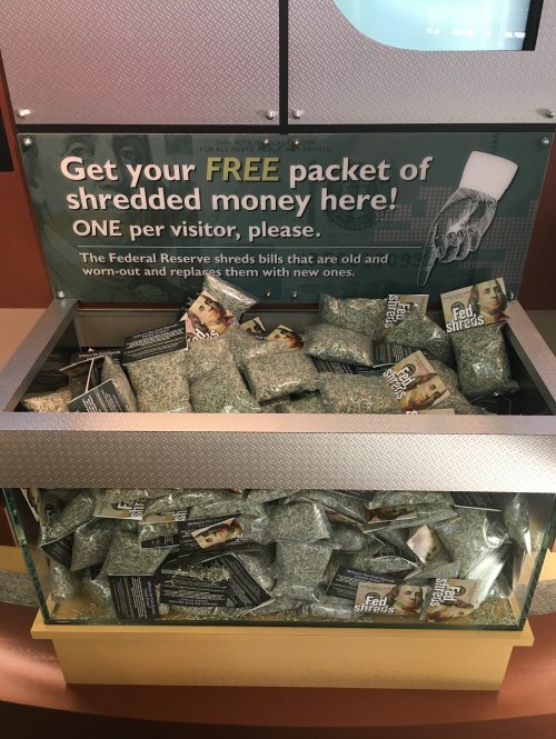 A display case filled with packets of shredded money, with a sign offering free samples to visitors.