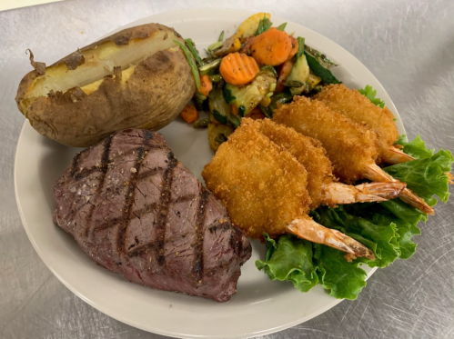 A plate featuring grilled steak, a baked potato, breaded shrimp, and mixed vegetables on a bed of lettuce.