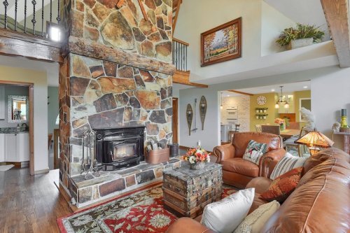 Cozy living room with a stone fireplace, leather sofas, and rustic decor, featuring a wooden beam ceiling and warm lighting.