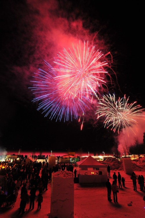 Colorful fireworks illuminate the night sky over a crowd gathered in a snowy landscape, celebrating an event.