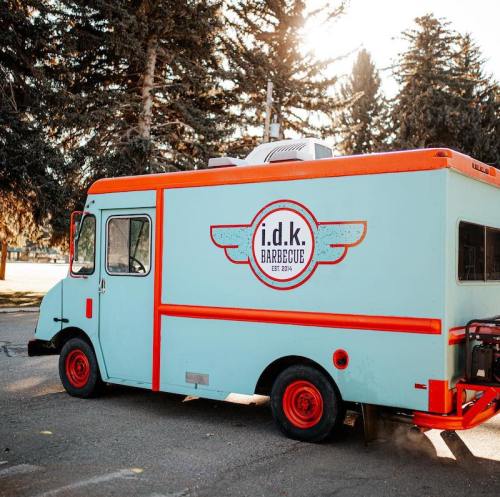 A colorful food truck with a light blue exterior and orange accents, featuring the logo "i.d.k. Barbecue" established in 1974.
