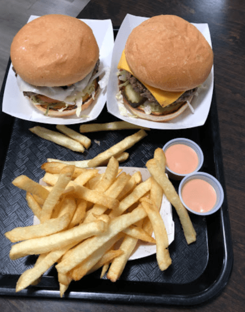 Two burgers on a tray with a side of golden French fries and two small cups of dipping sauce.