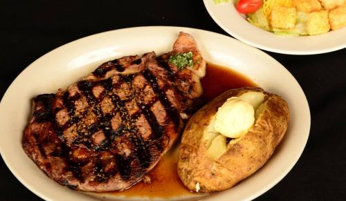 A grilled steak with seasoning, served with a baked potato topped with butter and a side salad.
