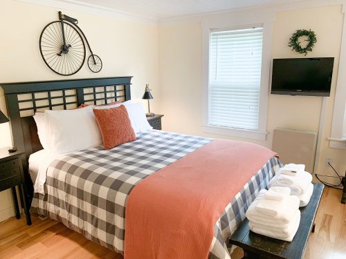 Cozy bedroom with a plaid bedspread, orange accents, and a bicycle wall decor. Features a TV and fresh towels on a bench.