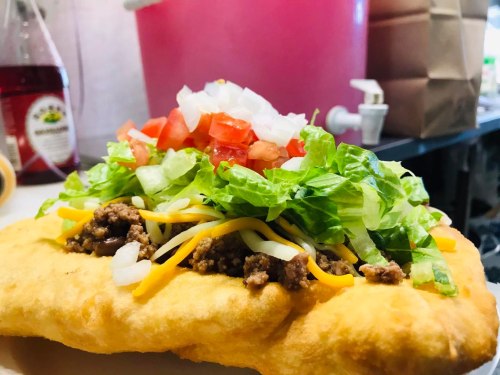 A close-up of a taco with ground beef, shredded cheese, lettuce, tomatoes, and onions on a crispy shell.
