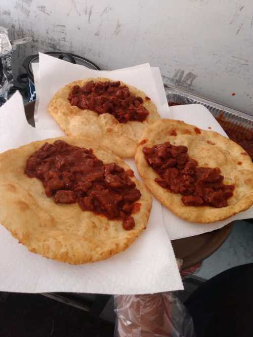 Three fried flatbreads topped with a rich, spicy meat sauce, served on a paper towel.