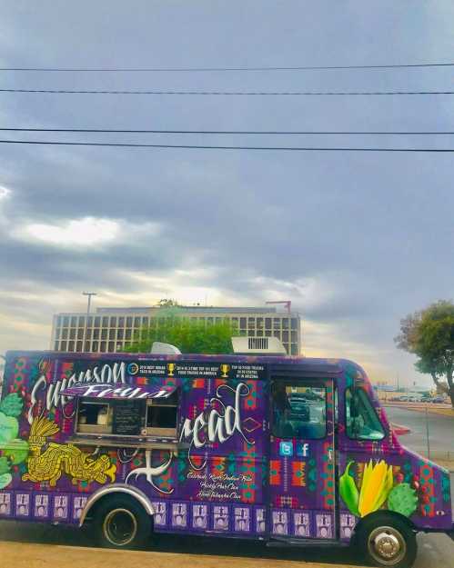 A colorful food truck with vibrant artwork parked under a cloudy sky, featuring the name "Simpson Road."