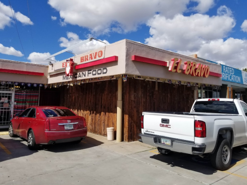 Exterior of El Bravo Mexican Food restaurant with a red car and a white truck parked outside under a blue sky.