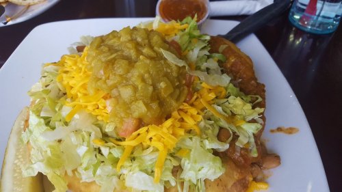 A plate of nachos topped with lettuce, cheese, green salsa, and a side of sauce.