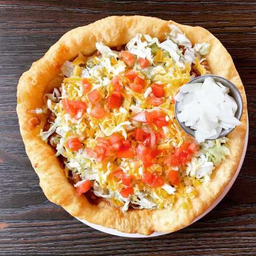 A crispy taco bowl filled with lettuce, tomatoes, cheese, and onions on a wooden table.