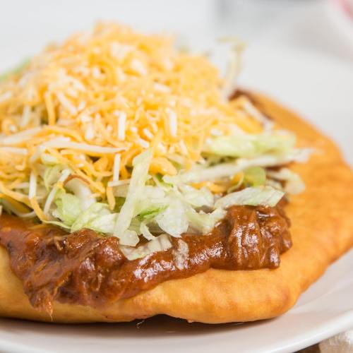 A close-up of a crispy taco shell topped with seasoned meat, shredded lettuce, and melted cheese.