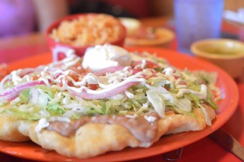 A colorful plate featuring a crispy flatbread topped with lettuce, tomatoes, onions, sour cream, and refried beans.