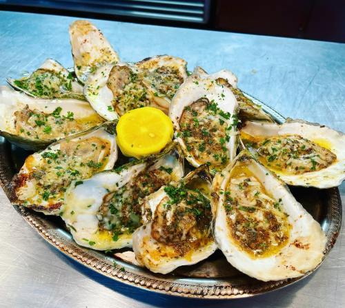 A platter of baked oysters topped with herbs and spices, garnished with a lemon slice.