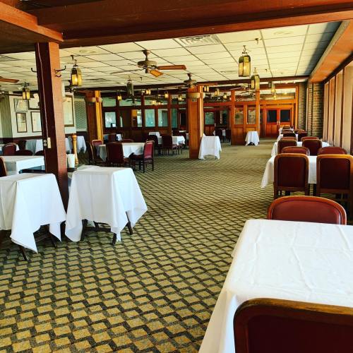 A spacious restaurant interior with empty tables covered in white tablecloths and wooden accents.
