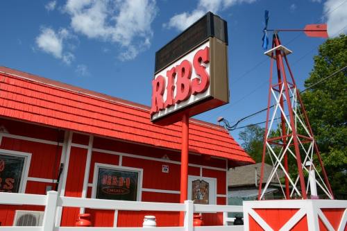 A red and white restaurant with a sign reading "RIBS" and a decorative windmill nearby under a blue sky.