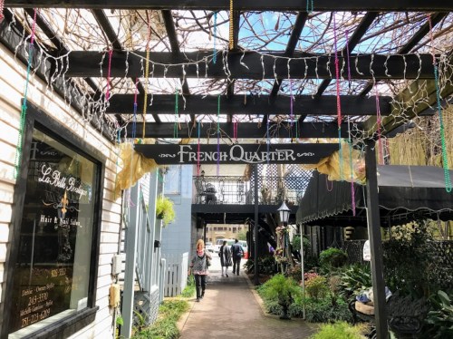 A charming walkway in the French Quarter, adorned with lights and beads, leading to shops and greenery.
