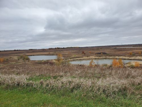 A cloudy landscape featuring two small ponds surrounded by grassy fields and autumn foliage.