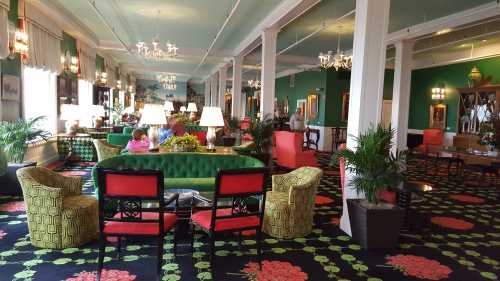 A vibrant hotel lobby with green and red decor, featuring plush seating, plants, and chandeliers.