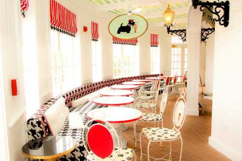 Bright café interior with curved seating, red and black decor, and elegant tables under striped window treatments.