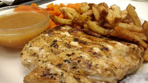 Grilled fish fillet with a side of fries, carrots, and a small bowl of sauce on a white plate.