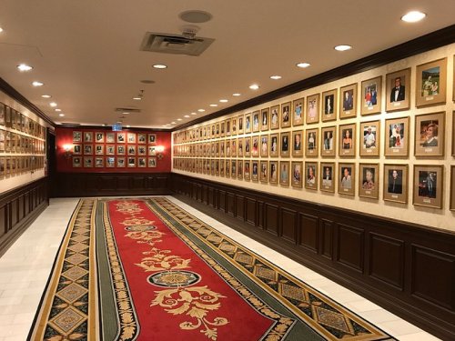 A hallway lined with framed portraits on the walls, featuring a decorative carpet in the center.