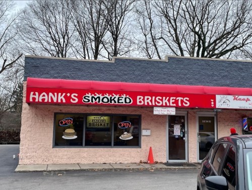 A storefront with a red awning reading "Hank's Smoked Briskets," featuring large windows and an "Open" sign.
