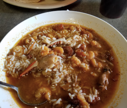 A bowl of seafood gumbo with rice, featuring shrimp, crab, and spices, served with a spoon.
