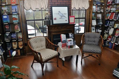 Cozy reading nook with two chairs, a small table, and a framed bird print, surrounded by bookshelves.