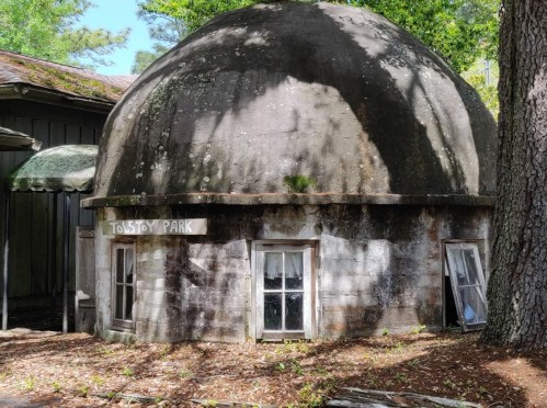 A weathered, dome-shaped structure with a sign reading "Tolstoy Park," surrounded by trees and fallen leaves.