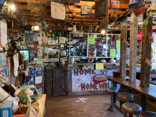 A cozy, eclectic bar interior filled with colorful decor, signs, and a rustic wooden counter.