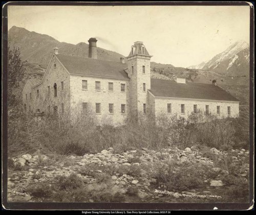 Historic stone building surrounded by trees and mountains, captured in black and white.