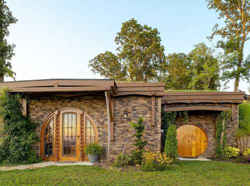 A charming stone house with a green roof, featuring arched wooden doors and surrounded by lush greenery.