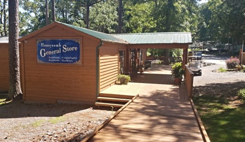 A wooden general store with a green roof, surrounded by trees and a wooden walkway leading to the entrance.